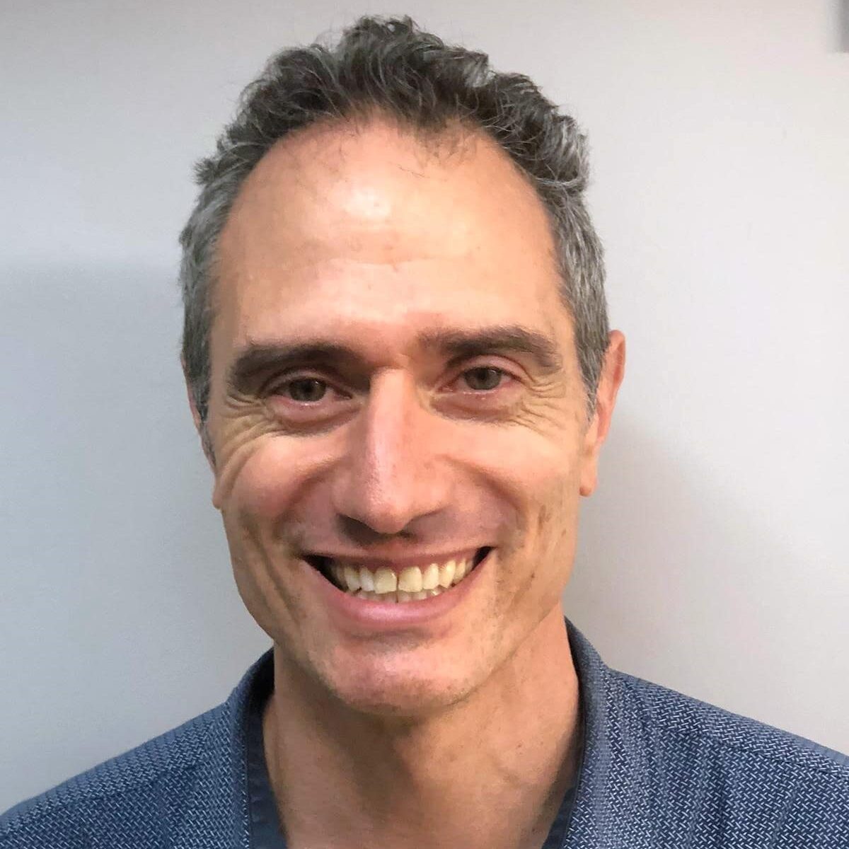 head shot of a white man wearing a blue collared shirt smiling